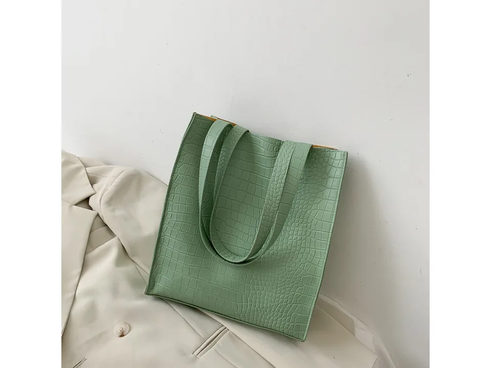 Light green crocodile pattern tote bag resting on a beige blazer.