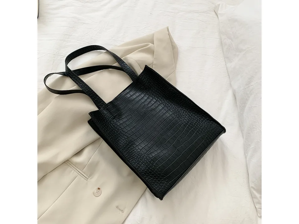 Black crocodile pattern tote bag resting on a beige blazer.