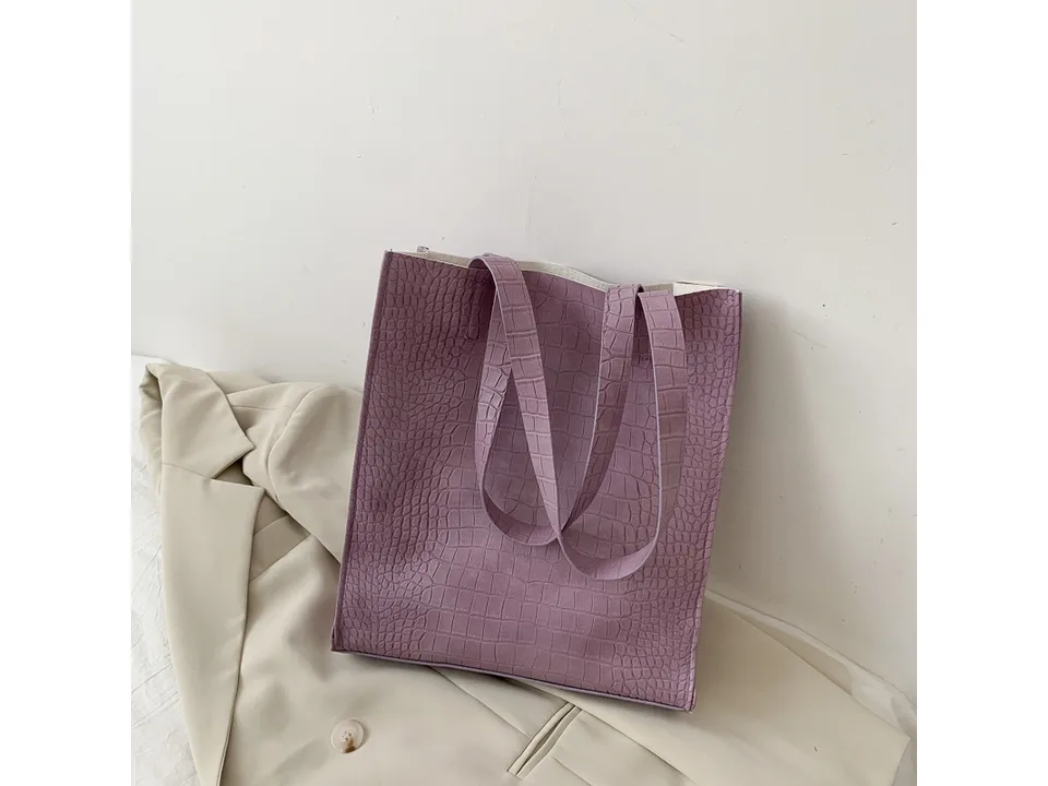 Purple crocodile pattern tote bag resting on a beige blazer.