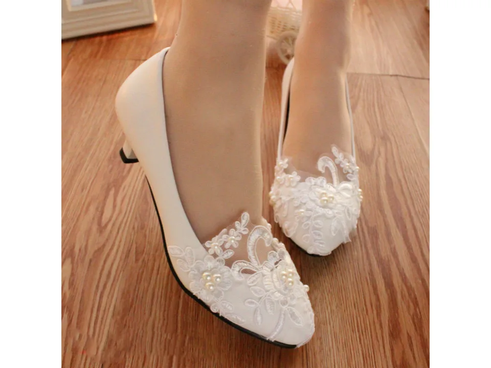 Close-up of feet wearing white lace wedding shoes with pearl details.