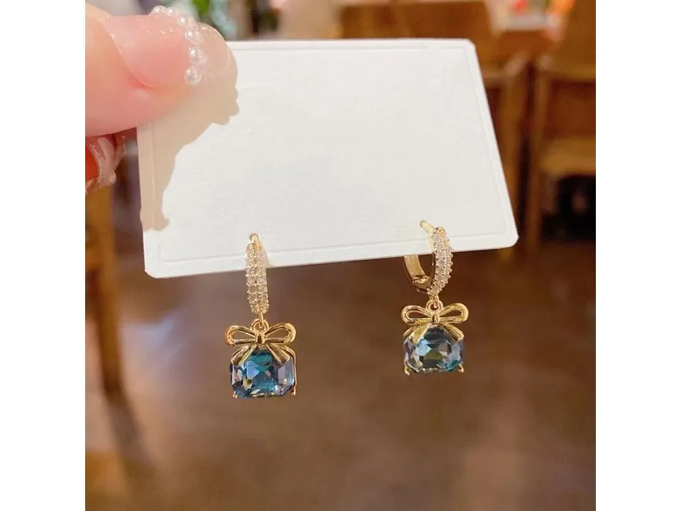Pair of bow and blue crystal drop earrings on a white display card.