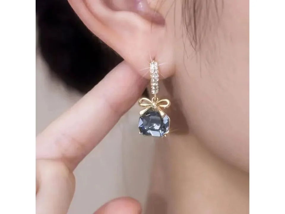 Close-up of the bow and blue crystal earring worn on an ear.