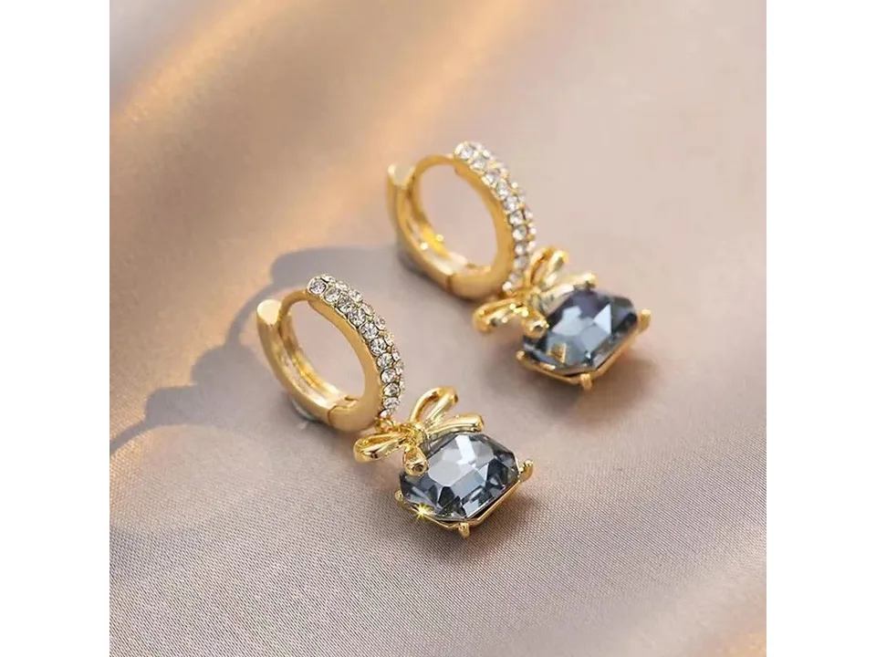 Angled view of the bow and blue crystal drop earrings on a soft surface.
