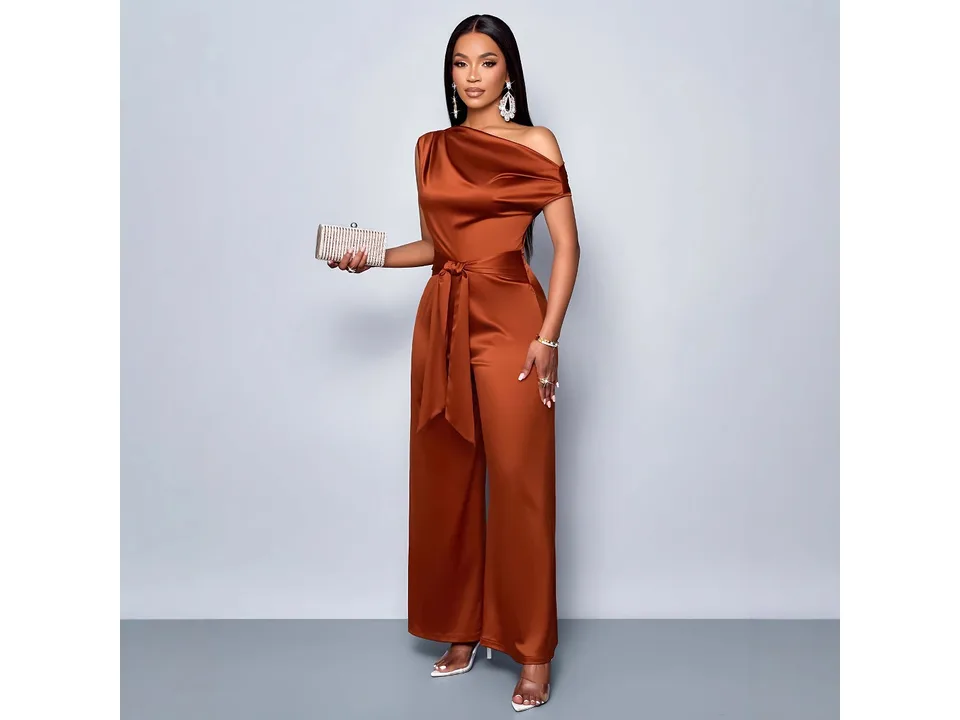 Model wearing the rust-colored one-shoulder jumpsuit and holding a small clutch bag.