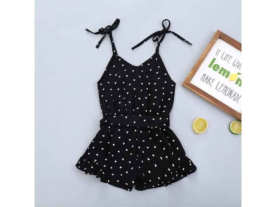 Black girls' jumpsuit with white heart print, tie straps, and ruffle hem, displayed flat.