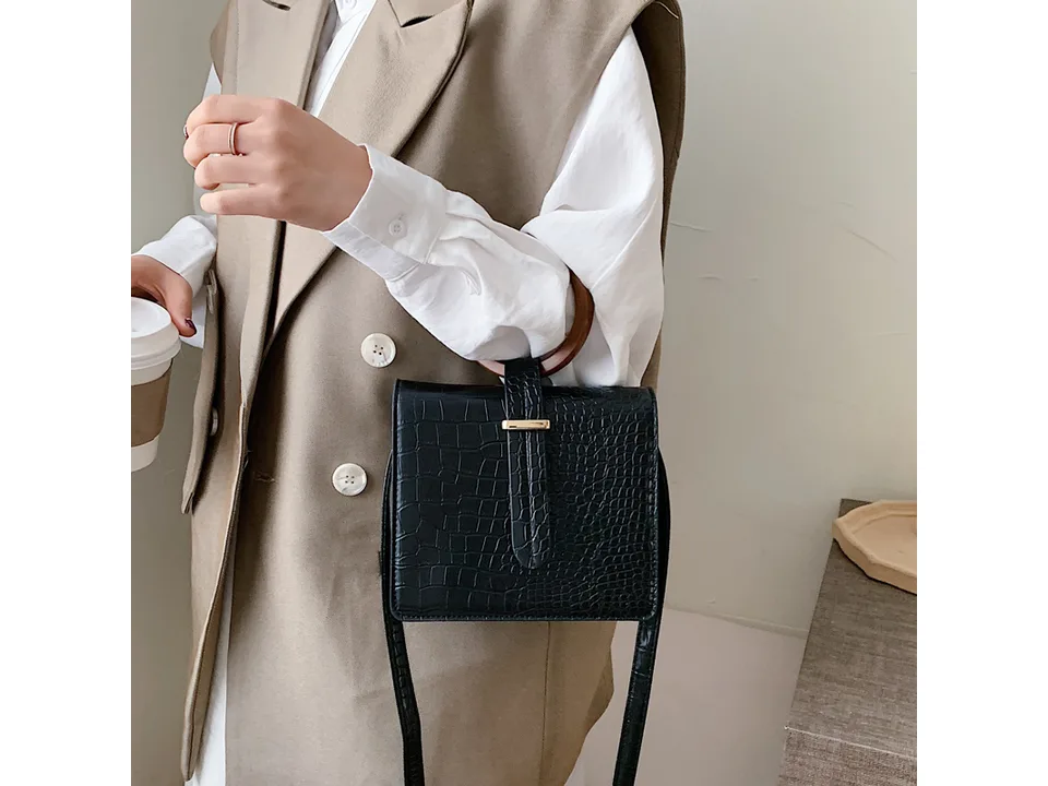 Close-up of a hand holding a black crocodile-patterned bag with a round wooden handle.