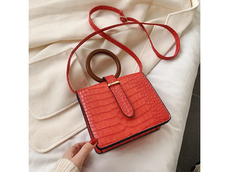 A red crocodile-patterned messenger bag with a round wooden handle.