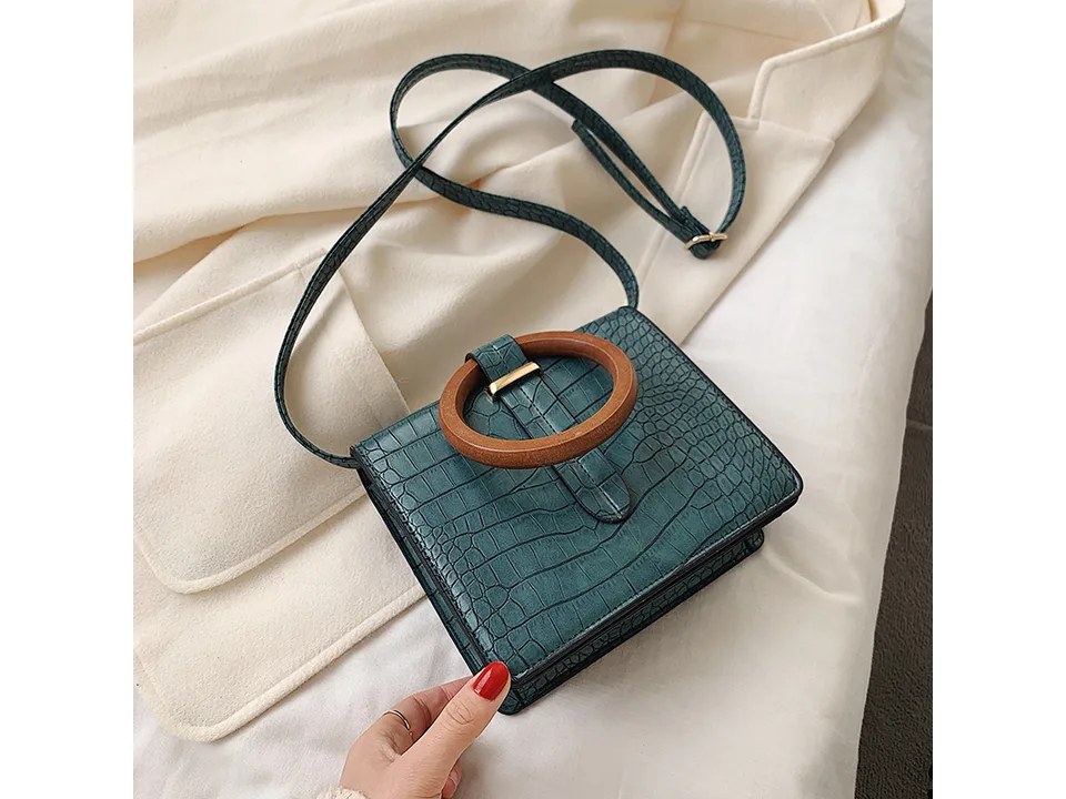 A green crocodile-patterned messenger bag with a round wooden handle.