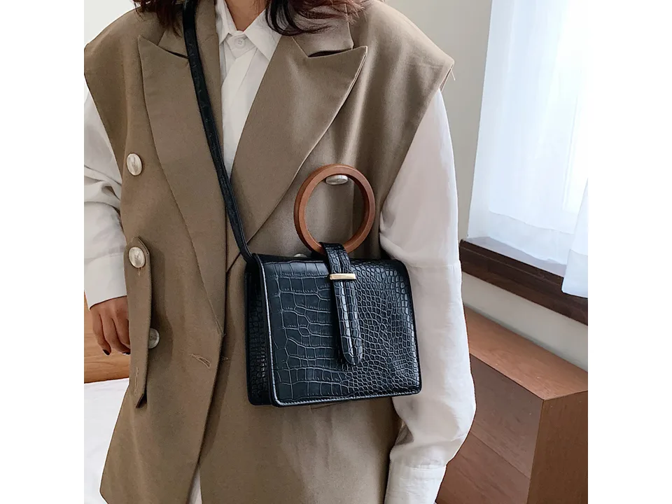 A woman wearing a black crocodile-patterned messenger bag with a round wooden handle.