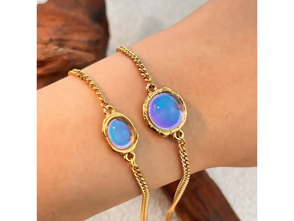 Two gold chain bracelets with round, iridescent gemstones worn on a wrist.
