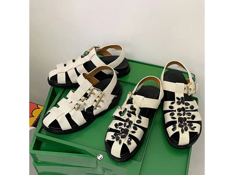 A pair of white closed-toe sandals with black rhinestone embellishments on a green surface.