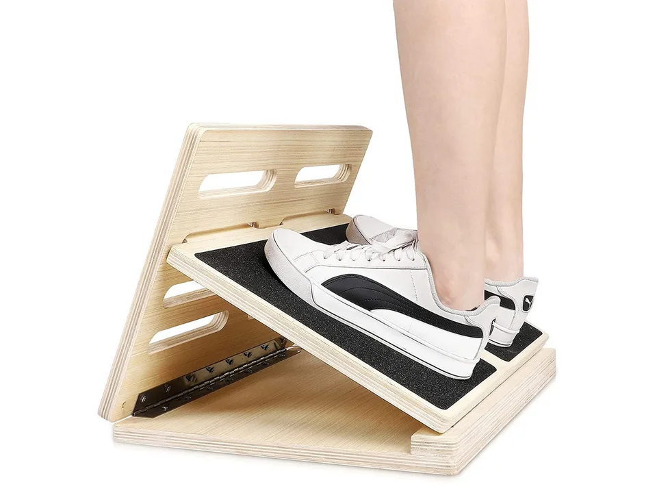 Side view of a person standing on the wooden slant board with athletic shoes.