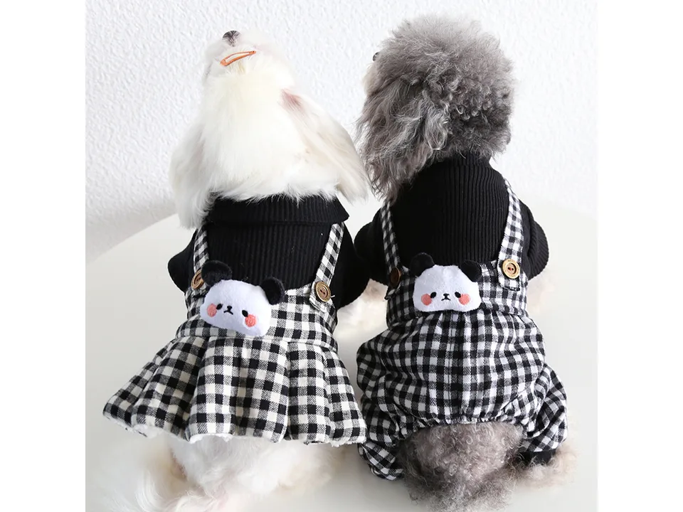 Two dogs wearing black and white plaid pet clothes with panda details.