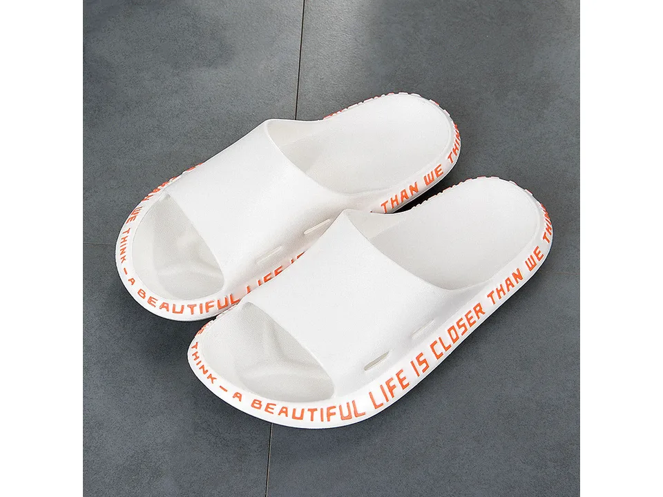 A pair of white slide sandals with orange text on the side.