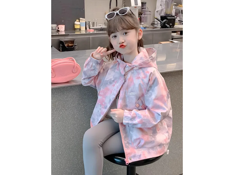 A young girl wearing a pink and grey tie-dye hooded windbreaker jacket.