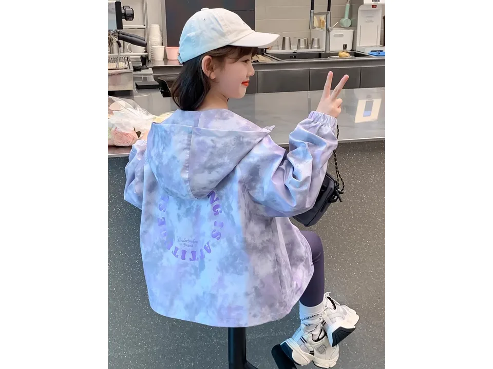 A young girl wearing a purple and grey tie-dye hooded windbreaker jacket, seen from the back.