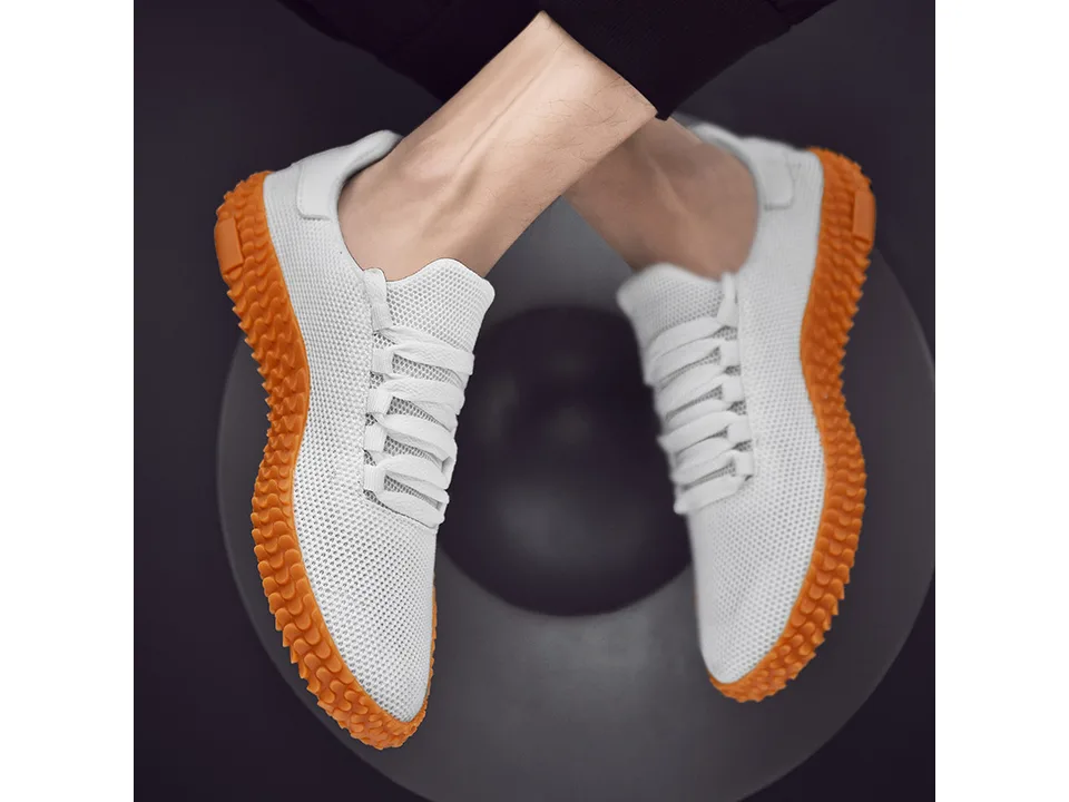 A pair of white low-top sneakers with orange textured soles worn on feet.