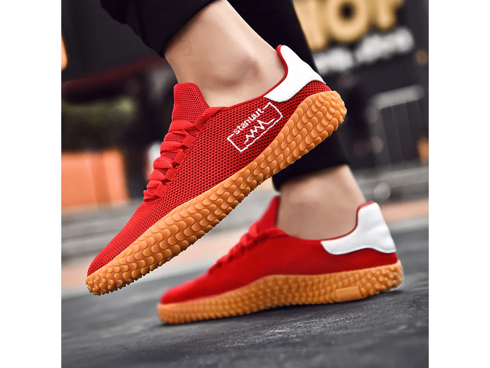 A pair of red low-top sneakers with orange textured soles worn on feet.