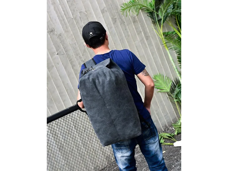 A man wearing a dark grey canvas backpack, showing the back view.