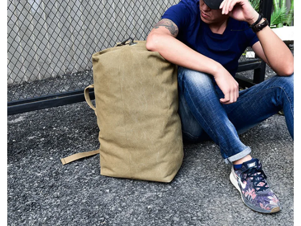 A man sitting on the ground next to the khaki canvas backpack.