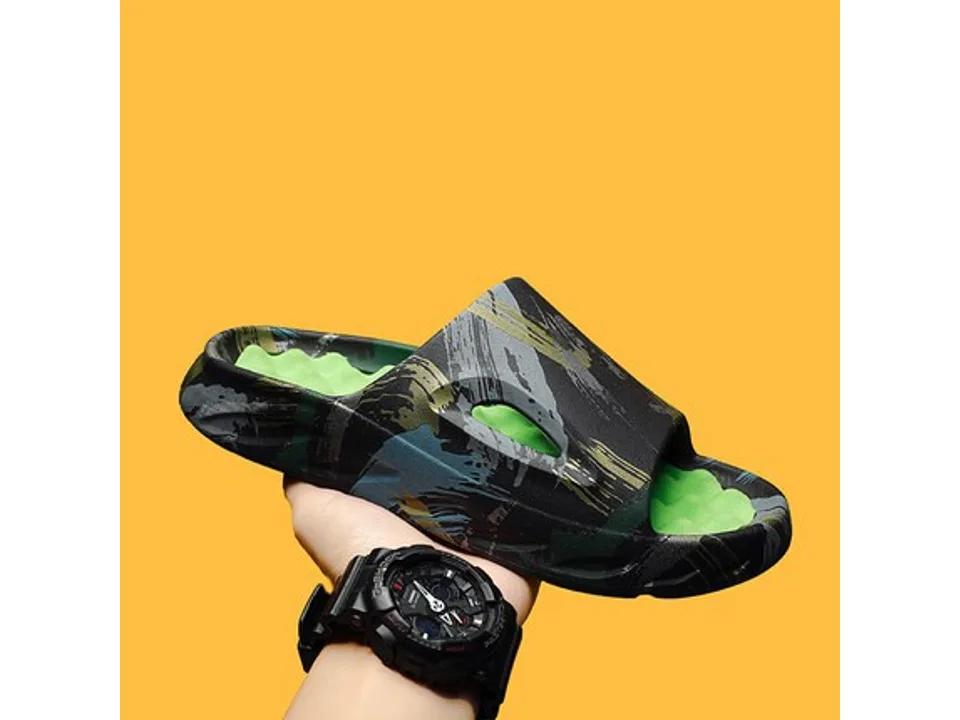 A black and green abstract print slide sandal with a green textured footbed, held in a hand.