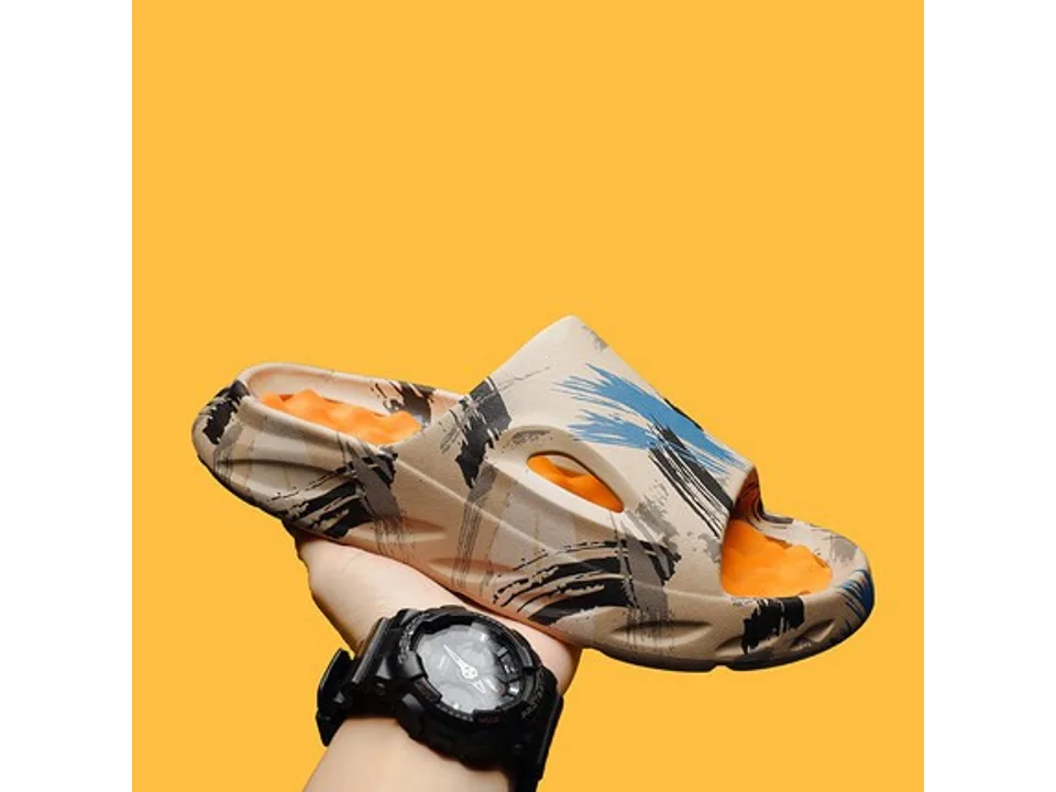 A beige and blue abstract print slide sandal with an orange textured footbed, held in a hand.