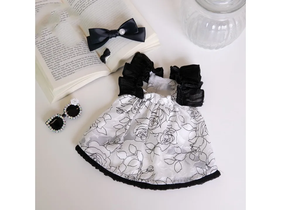 The floral chiffon dog dress laid flat on a table next to a bow and sunglasses.