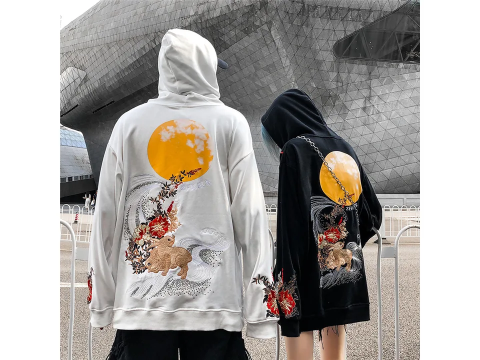 Two people wearing white and black hoodies with rabbit and moon embroidery.