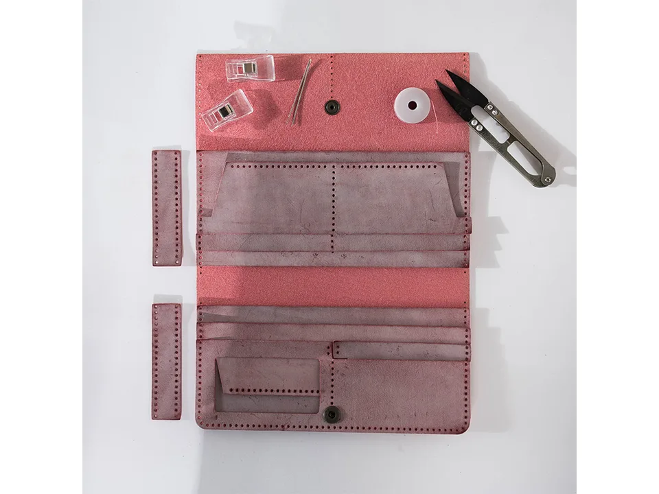 A DIY leather wallet kit laid out with pre-cut leather pieces, needles, thread, and clips.
