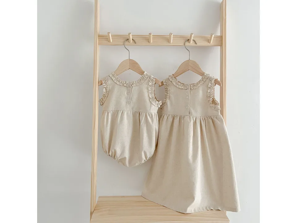 A baby romper and a matching dress hanging on a wooden rack.