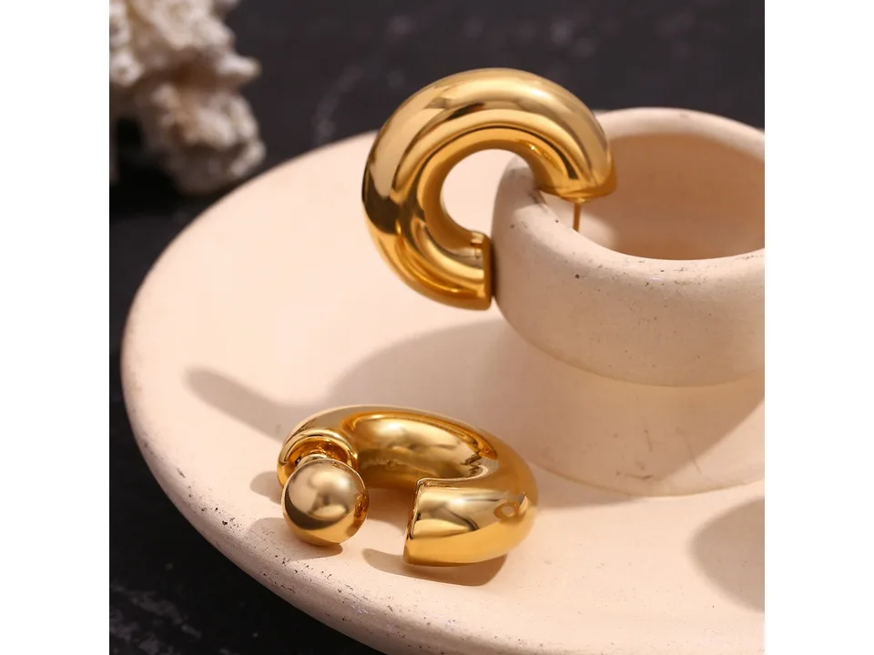 Gold-tone hollow tube ball stud earrings resting on a small ceramic dish.