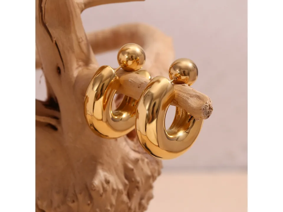 Gold-tone hollow tube ball stud earrings displayed on a piece of driftwood.