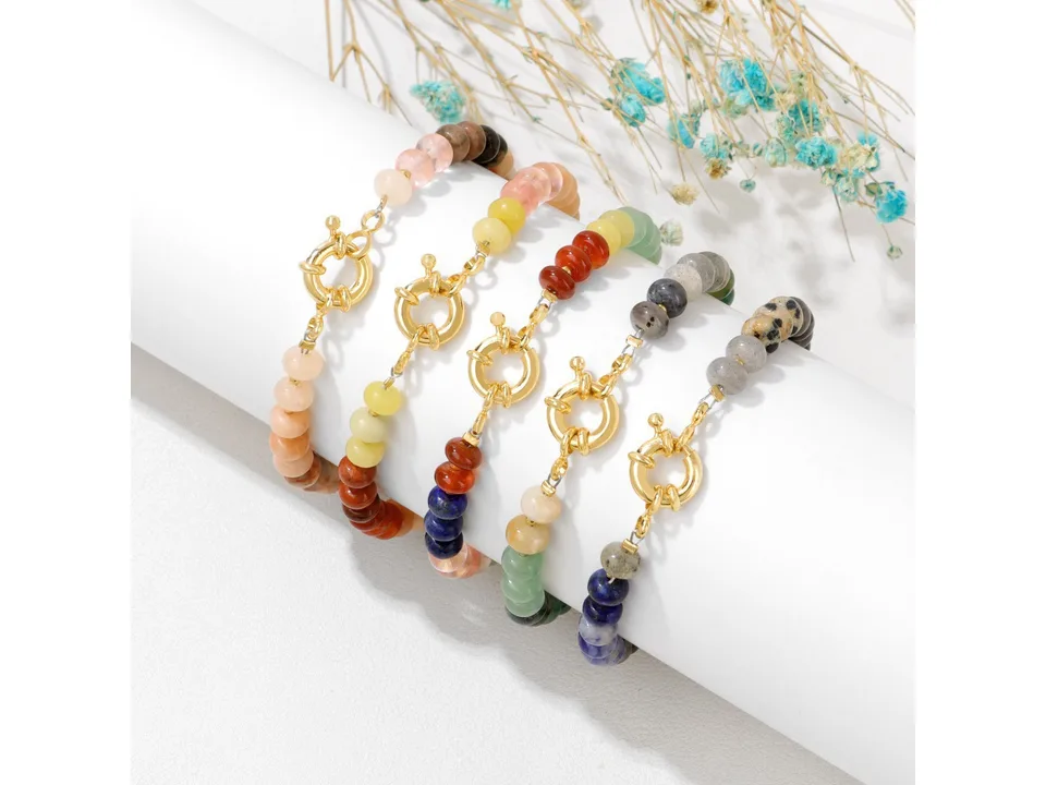 Five different styles of stone bead bracelets displayed together on a white stand.