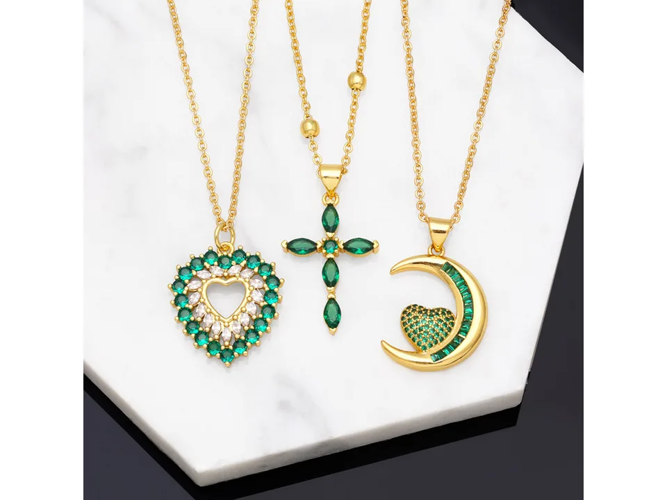 Three gold necklaces with green stone pendants shaped like a heart, a cross, and a crescent moon.