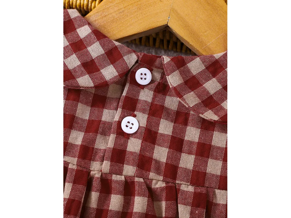 Close-up of the white buttons on the front of the plaid baby romper.