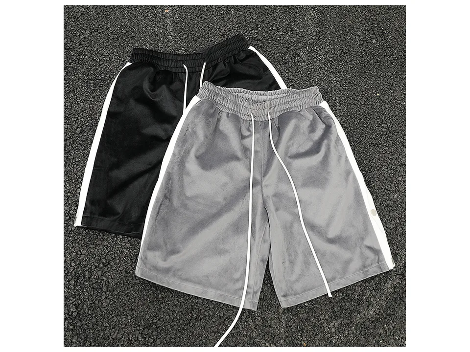Black and grey athletic shorts with white side stripes and snap buttons laid out on the ground.
