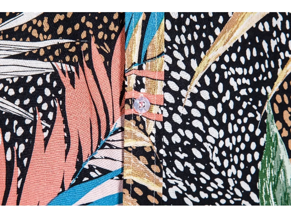 Close-up of the shirt fabric showing the tropical leaf pattern and a button.