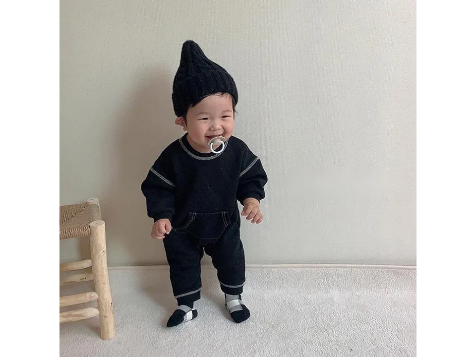 A baby wearing the black long sleeve romper with contrast stitching.