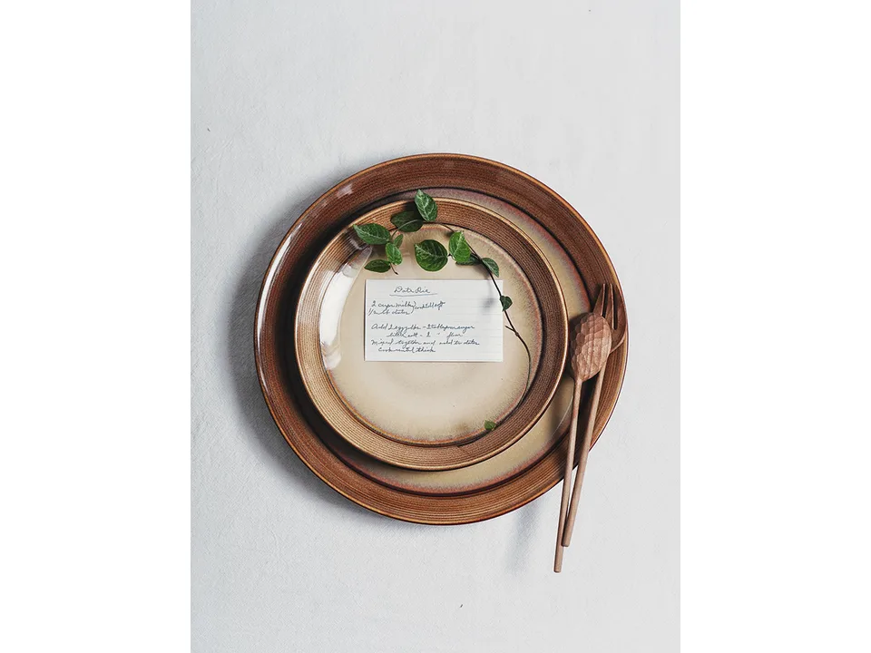 A ceramic dish with a recipe card and wooden utensils on a white tablecloth.