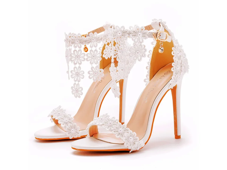 A pair of white floral high-heeled sandals with tassel details on a white background.