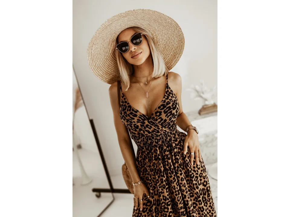 A woman wearing a leopard print maxi slip dress with a straw hat.