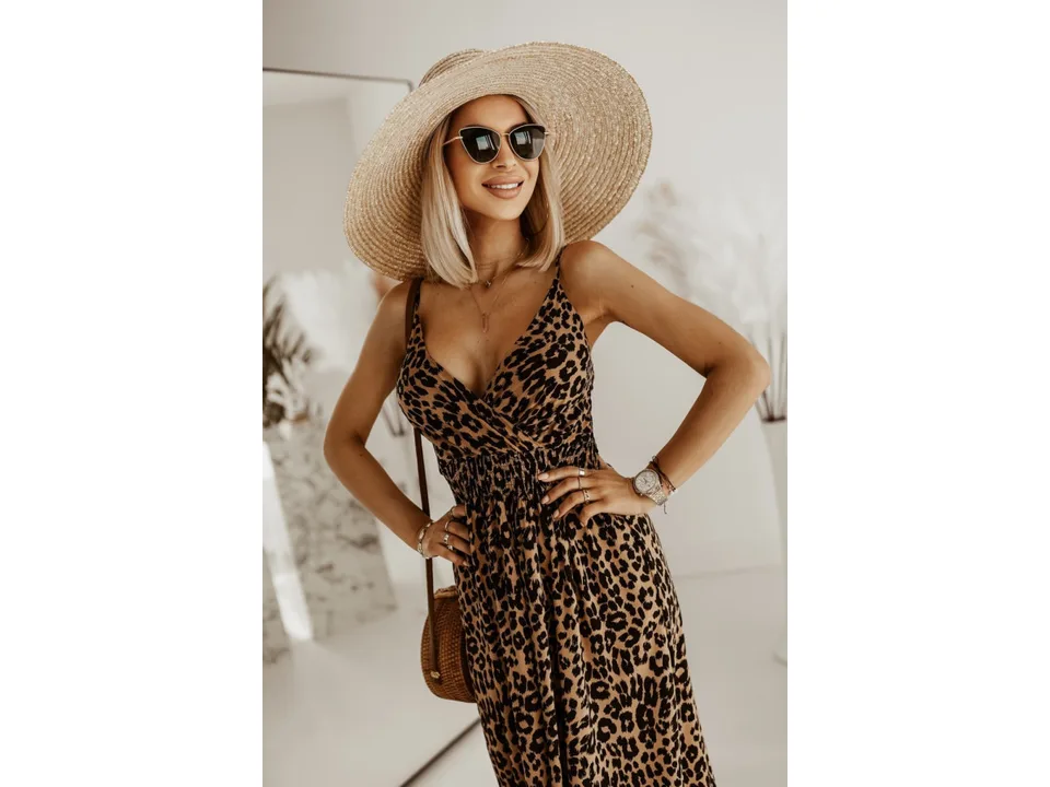 A woman posing in a leopard print maxi slip dress with a straw hat.