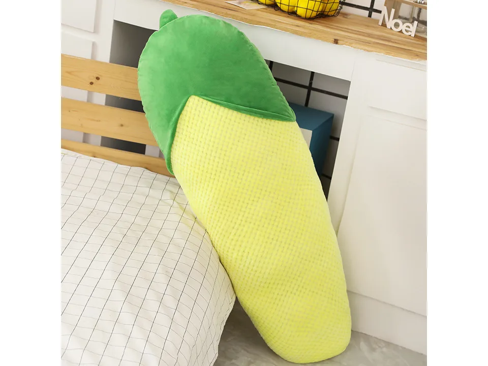 A corn-shaped plush pillow standing against a bed.