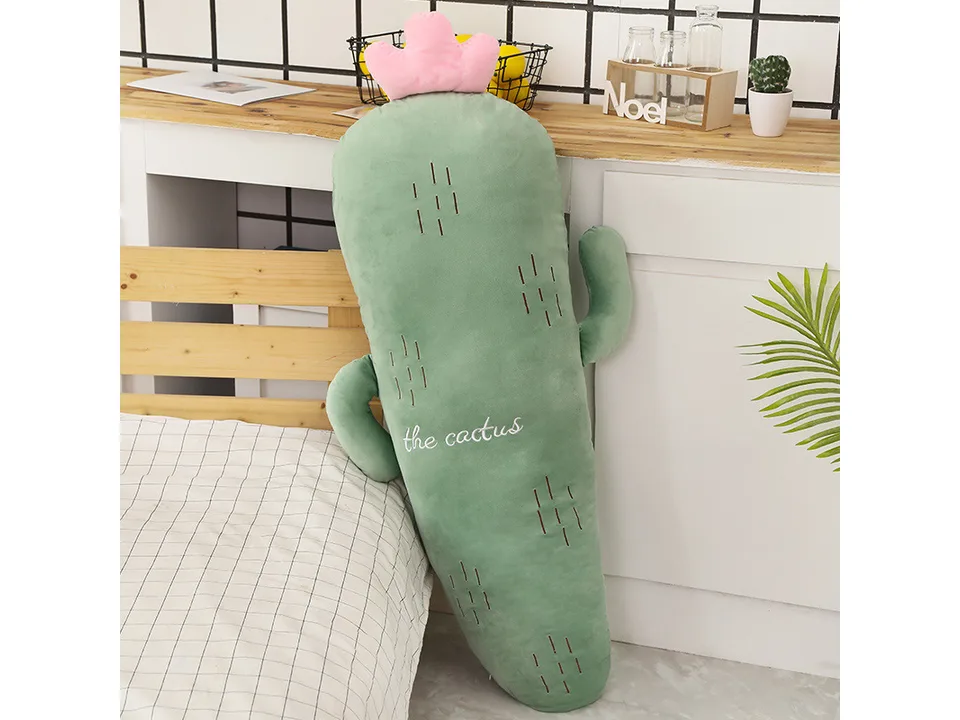 A cactus-shaped plush pillow standing against a bed.
