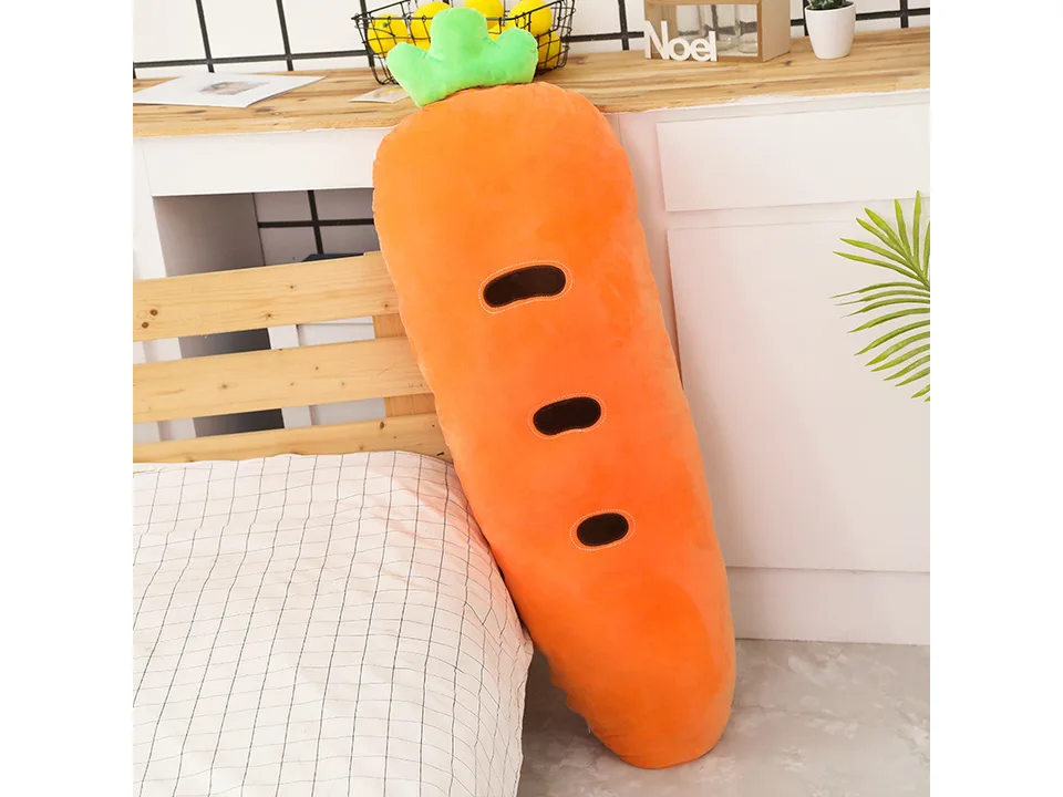 A carrot-shaped plush pillow standing against a bed.