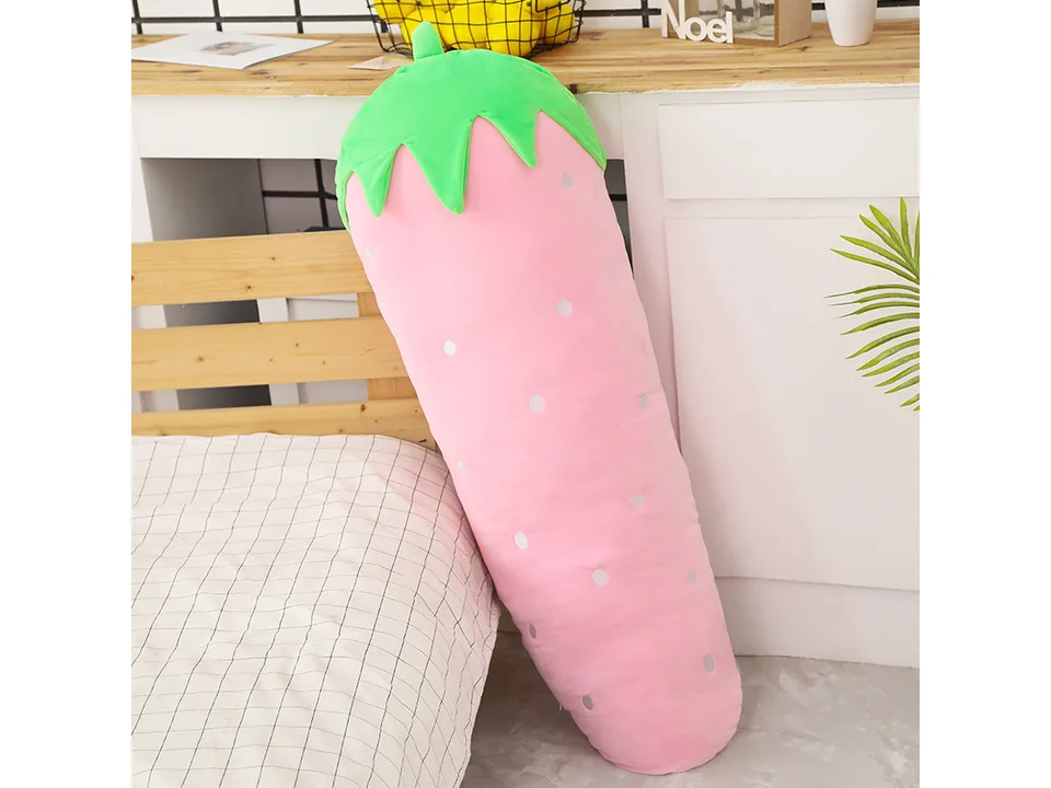 A pink strawberry-shaped plush pillow standing against a bed.