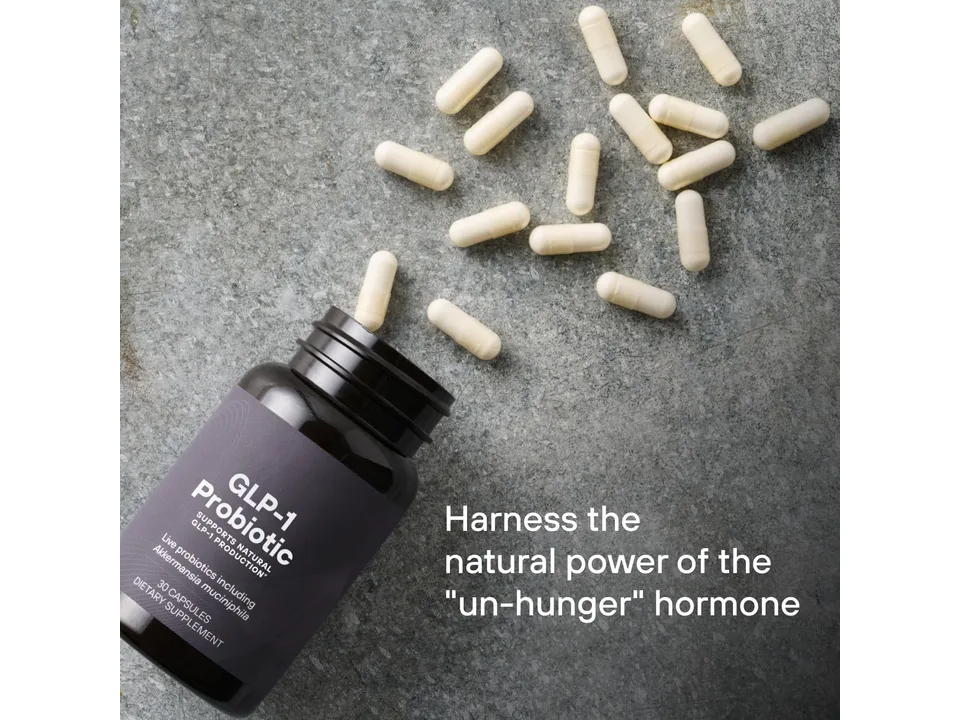 The probiotic supplement bottle with capsules spilled out on a stone surface.