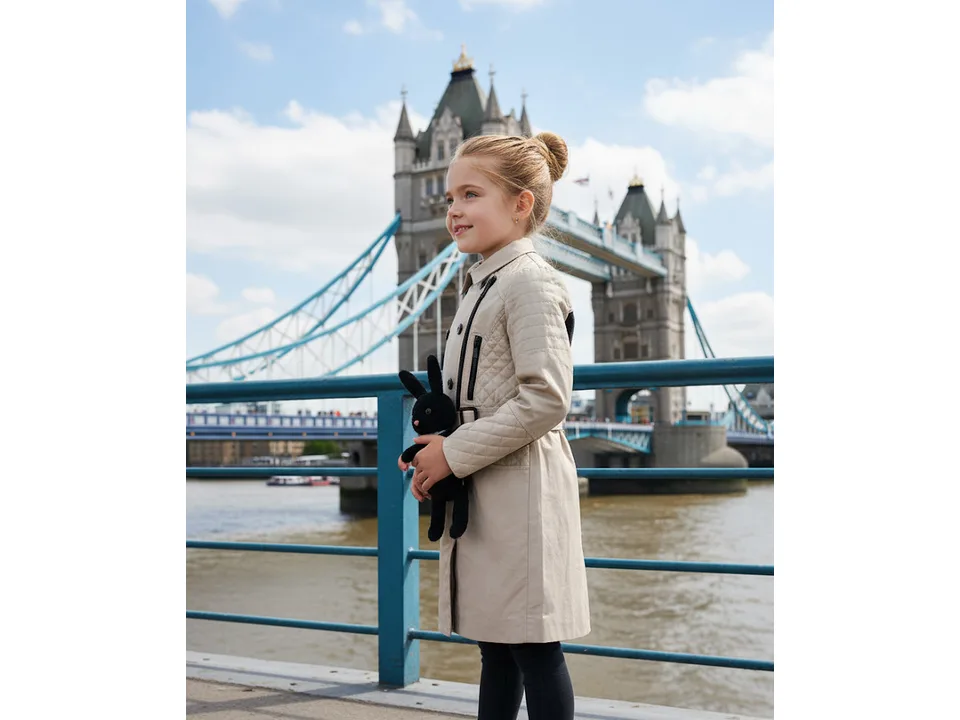 A young girl wearing the beige trench coat outdoors.