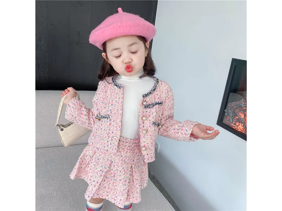 A young girl wearing a pink tweed jacket and pleated skirt set with a pink beret.