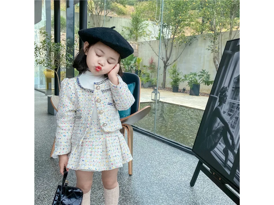 A young girl wearing a tweed jacket and pleated skirt set with a black beret.